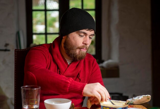 A man in a hat and sweater has breakfast in the kitchen