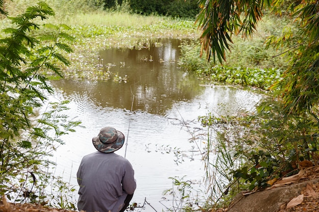 A man in a hat throws a fishing rod on a small pond