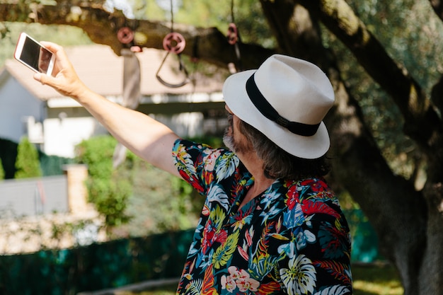 정원에서 셀카를 만드는 꽃 프린트 셔츠와 남자 모자
