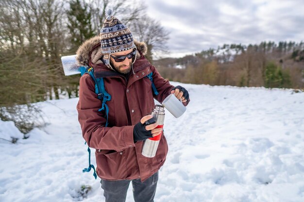 トレッキングを開始する前に、雪の中で冬に魔法瓶からホット コーヒーを朝食を持つ男