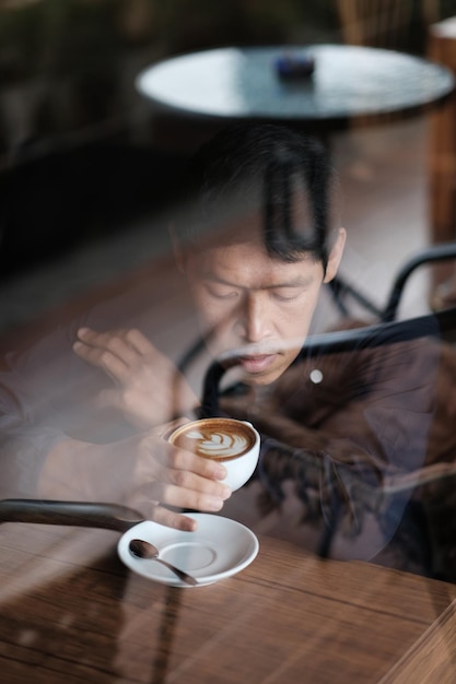 Uomo che beve caffè visto attraverso una finestra di vetro