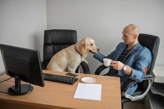 Foto uomo che beve caffè mentre guarda il cane vicino alla scrivania in ufficio