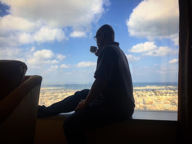 Photo man having coffee while sitting on window at home