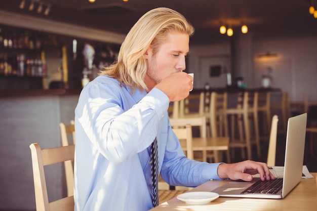 ラップトップを使用しながらコーヒーを飲んでいる男