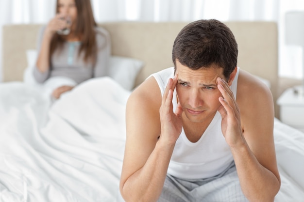 Человек с головной болью, сидящим на кровати со своей девушкой