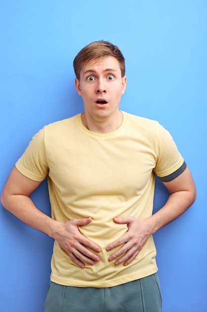 Man having painful stomach ache, chronic gastritis or abdomen bloating, stand in shock, he urgently needs to go to the toilet. isolated blue background