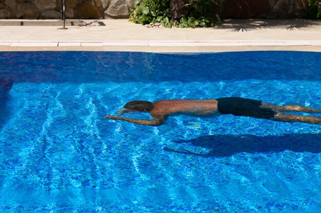 Foto un uomo in costume da bagno in stile hawaiano nuota sott'acqua in una pozza di acqua blu. il concetto di divertimento in piscina in vacanza.