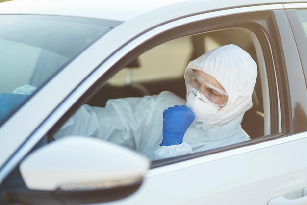 Man in Hazmat suit, protective gloves and goggles driving car during an epidemic in quarantine city.