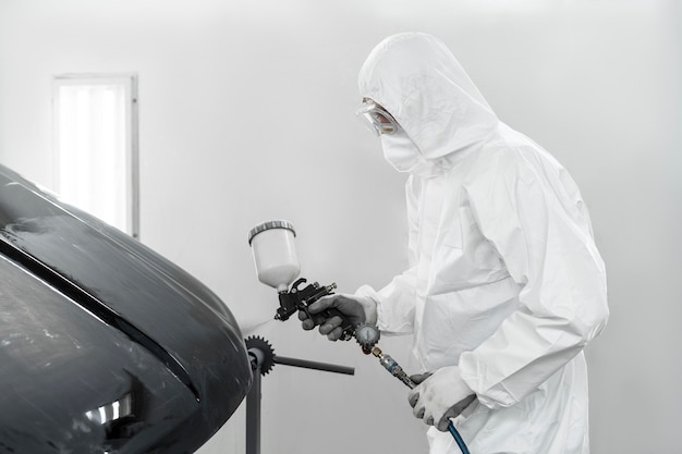 Photo man in hazmat suit using gun to paint car in the shop