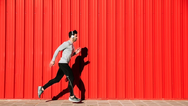 man in headphones running near red walll