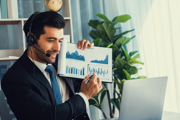 A man in a headset holds a graph on a laptop.