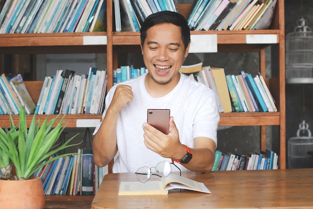 Man heeft goed nieuws van mobiele telefoon bij het lezen van een boek In bibliotheek Gelukkige uitdrukking