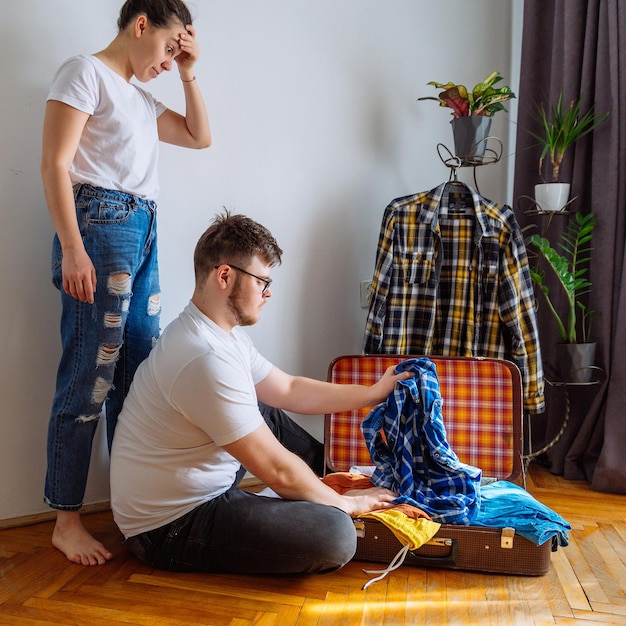 Man heeft hulp van een vrouw nodig bij het inpakken van reisconcept man probeert geschikte kleding in een reistas