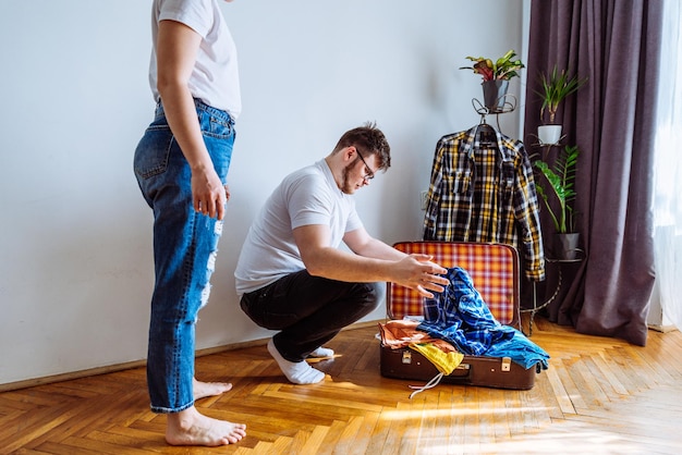 Man heeft hulp van een vrouw nodig bij het inpakken van reisconcept man probeert geschikte kleding in een reistas