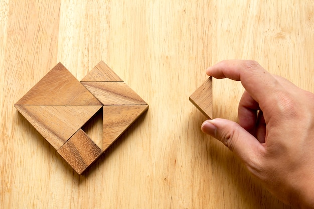 人は木製のテーブルの心の形を満たすためにtangramのパズルの一部を保持