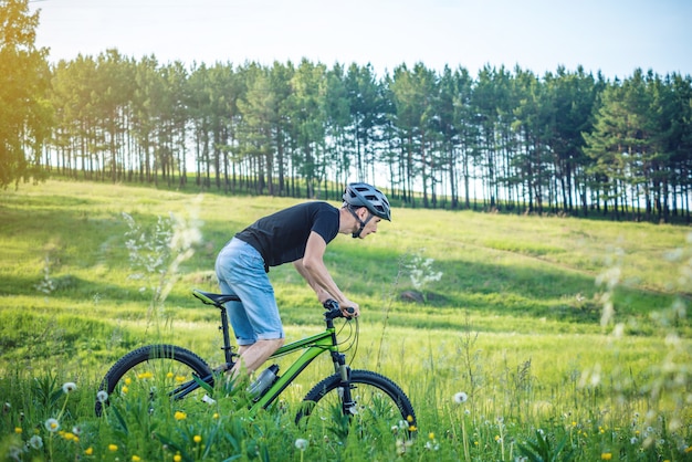 Man in a helmet riding on a green mountain bike in the woods among the trees. Active and healthy lifestyle