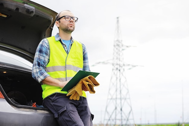 A man in a helmet and uniform, an electrician in the field. Professional electrician engineer inspects power lines during work.