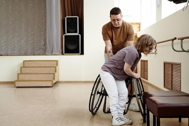 Man helping woman to take seat on wheelchair