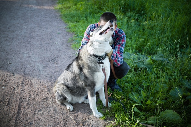 Man hiding behind a big gray dog near green lawn.