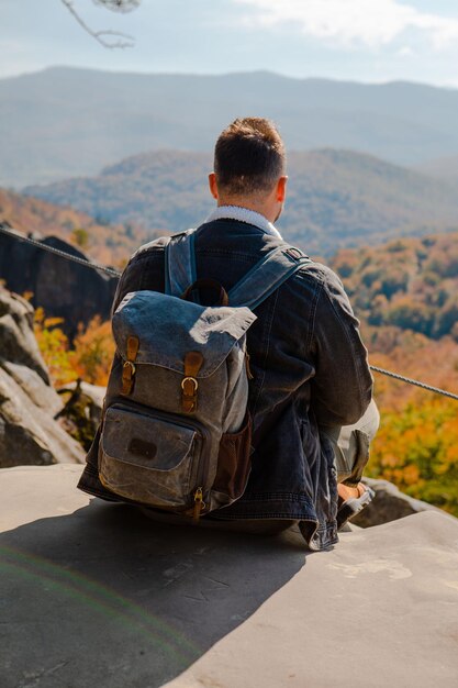 Man hiker sitting on the rock enjoying autumn landscape