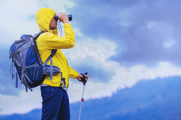 Man hiker with backpack traveling at mountain top looks at the view with binoculars