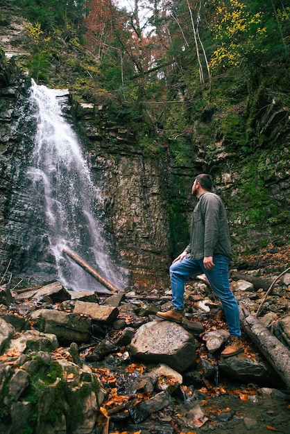 Concetto di escursionismo uomo guardando la cascata nella foresta di tuffo