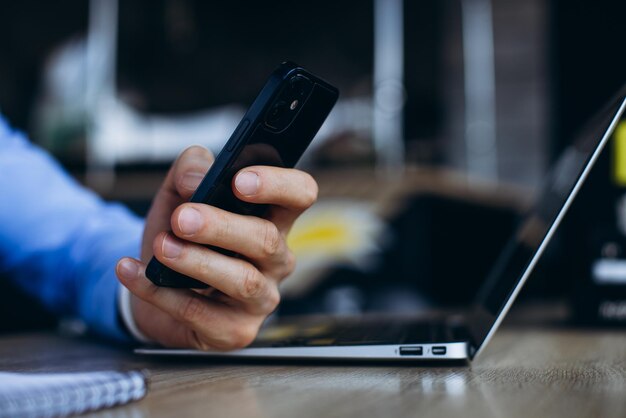 Man hilding phone close up photo and laptop on the table