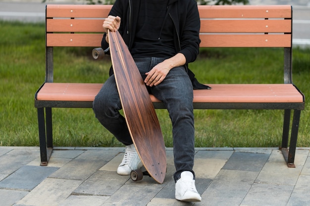 Man hipster resting sitting with skateboard or longboard on wooden bench