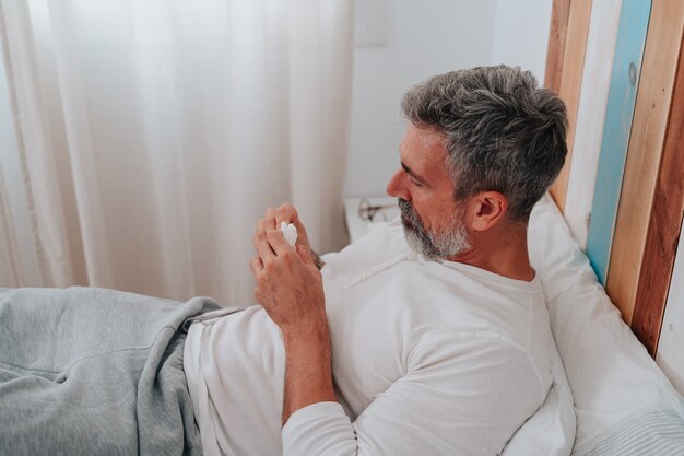 Uomo sulla cinquantina con i capelli grigi che prende il raffreddore mentre riposa nel suo letto
