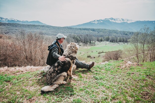 男と山を見て座っている彼の犬