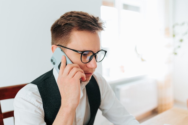 A man in his early s sitting in his home office talking with his boss on his smartphone he is a remo