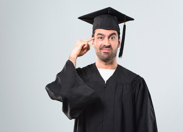 Man on his graduation day University making the gesture of madness putting finger on the h