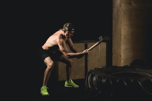 L'uomo colpisce la gomma. allenamento in palestra con martello e trattore siluet pneumatici