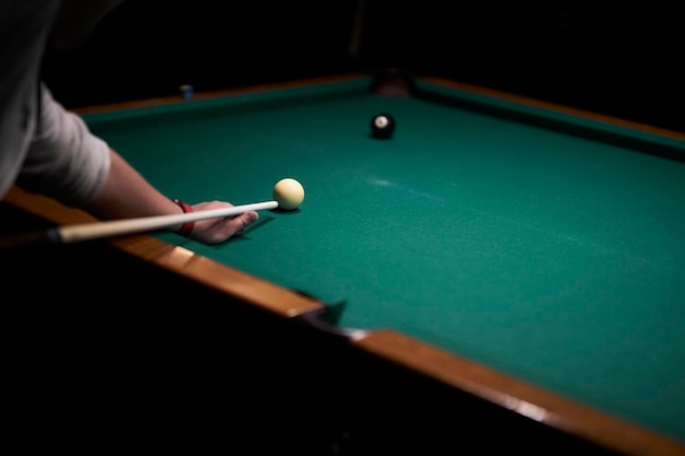 the man hits with a cue A hand with a cue aiming at a billiard ball at the table soft focus