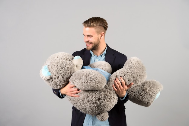 Man hold big teddy bear soft toy as present for birthday party on grey background. valentines day