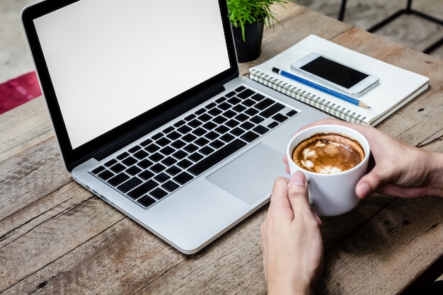 L'uomo tiene tazza di caffè con il computer portatile sul tavolo di legno