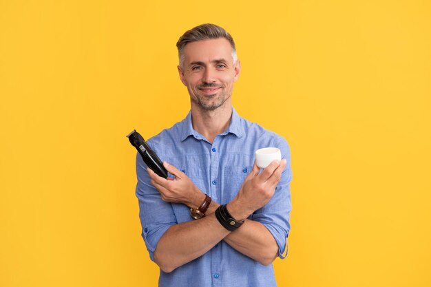 Man hold electric razor and cream on yellow background skin