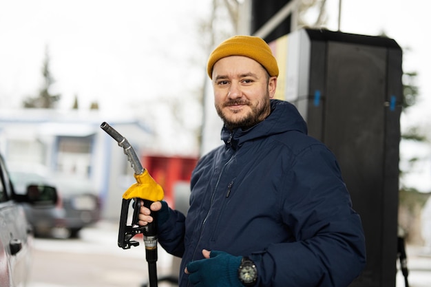 Photo man hold fuel pump while refueling his car at the gas station in cold weather