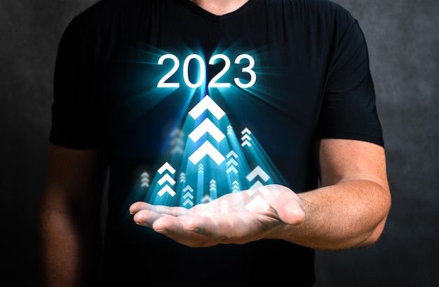 L'uomo tiene l'aumento delle frecce crescita futura anno 2023 lo sviluppo verso il successo e la motivazione la persona tiene l'ologramma con il 2023 le frecce in alto il successo aziendale e la crescita degli investimenti nel 2023