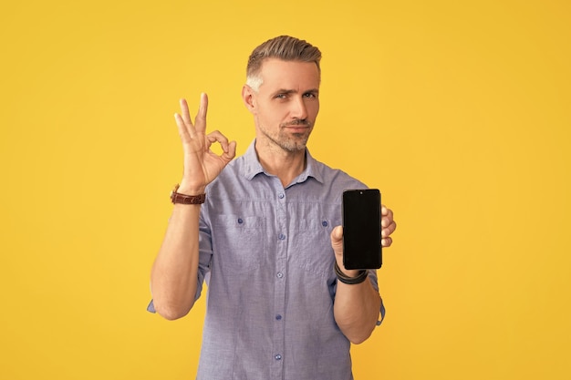 Man hold phone and show ok gesture on yellow background copy space advertisement