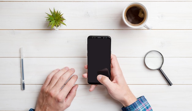 Man hold smart phone with blank screen for mockup Top views flat lay composition with white wooden desk in background