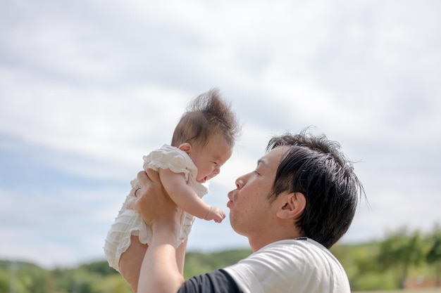 A man holding a baby in the air with the sky behind him