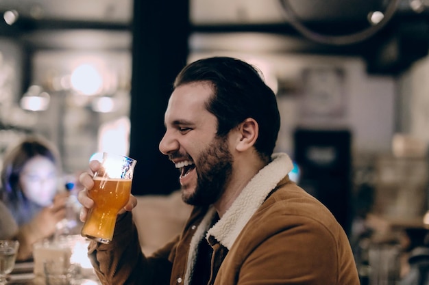 Photo man holding beer glass laughing while sitting in restaurant