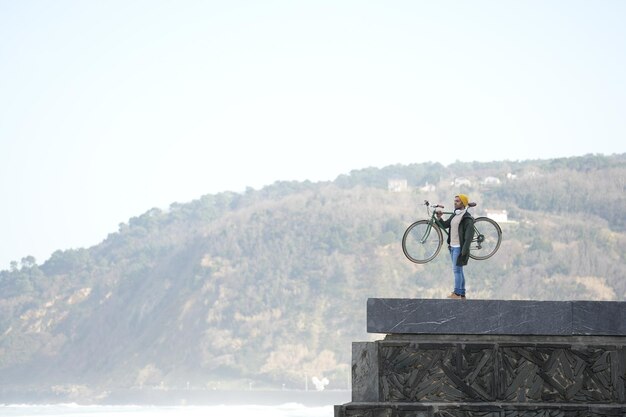 Man holding bicycle on shoulder on a wall looking landscape