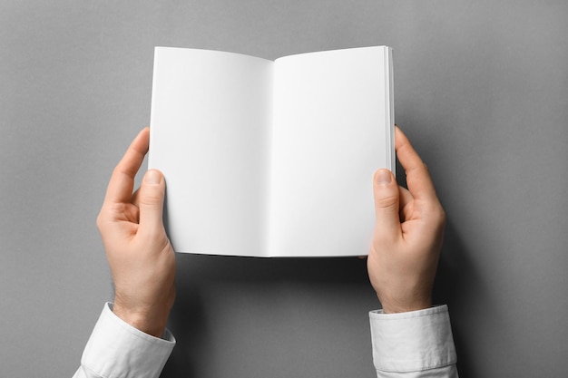 Man holding booklet with blank pages on grey background Mock up for design