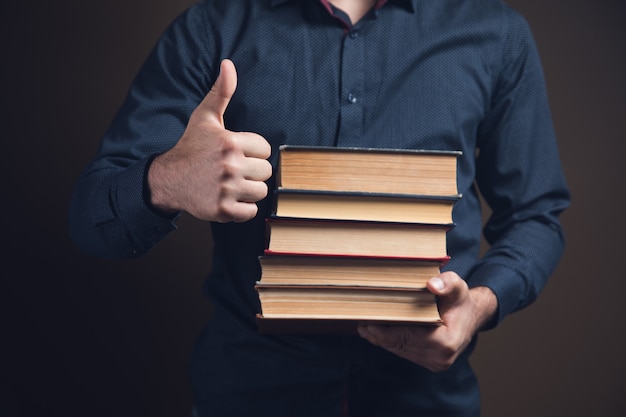 Мужчина держит книги и показывает палец вверх на коричневой поверхности