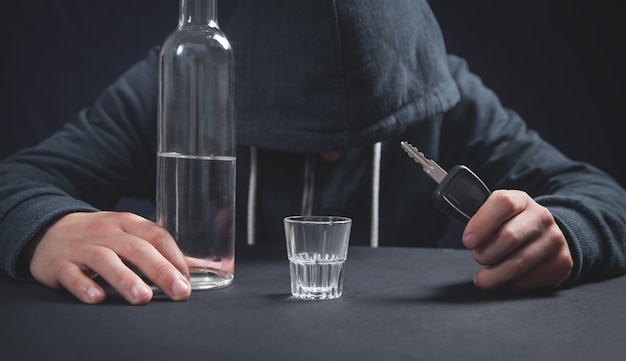 Man holding bottle of vodka and car key. Drunk driving