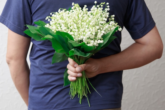 A man holding a bouquet of lilies of the valley for women. A man proposes.