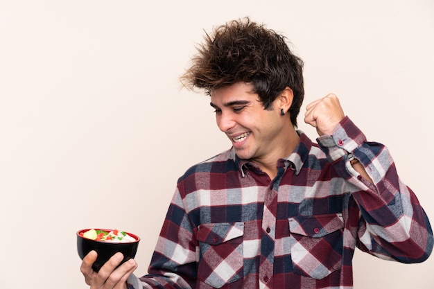 Man holding a bowl full of noodles celebrating a victory