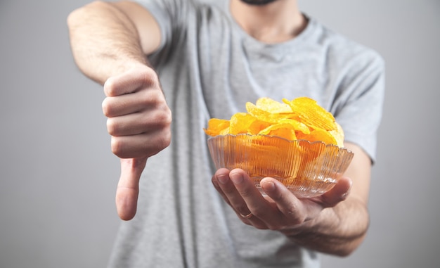 Man holding a bowl of potato chips and making thumb down.